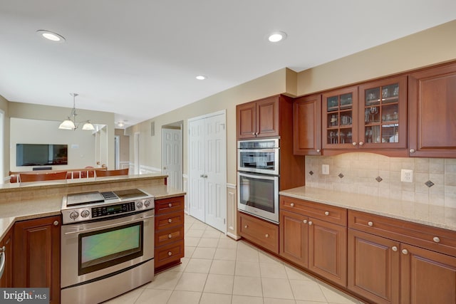 kitchen featuring light stone counters, light tile patterned flooring, appliances with stainless steel finishes, decorative backsplash, and glass insert cabinets