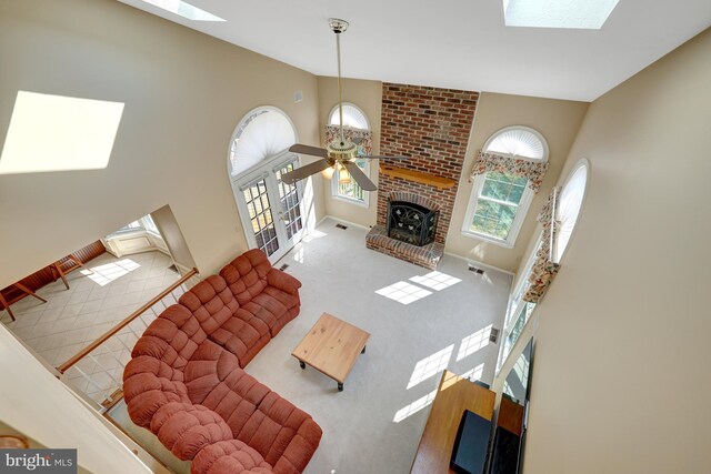 carpeted living room featuring a skylight, visible vents, a ceiling fan, a brick fireplace, and baseboards