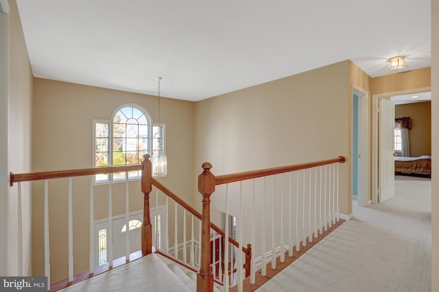 hallway with baseboards, carpet flooring, a notable chandelier, and an upstairs landing