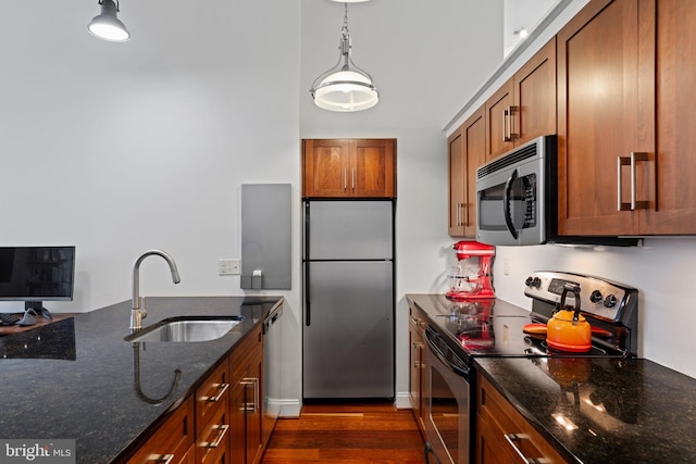 kitchen with appliances with stainless steel finishes, brown cabinets, dark stone countertops, hanging light fixtures, and a sink