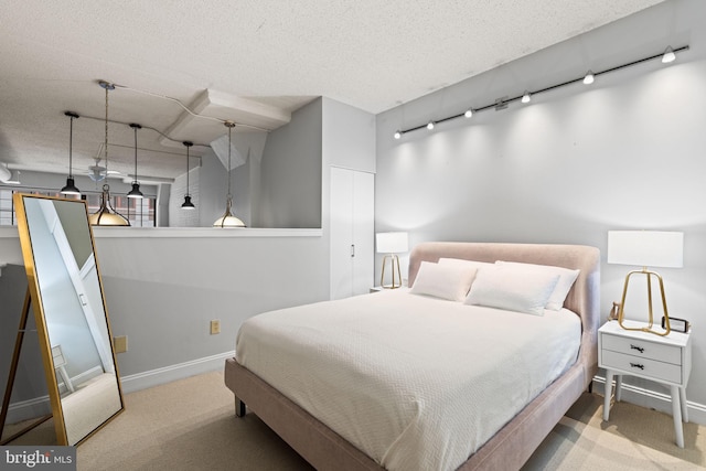 carpeted bedroom with a textured ceiling, rail lighting, and baseboards