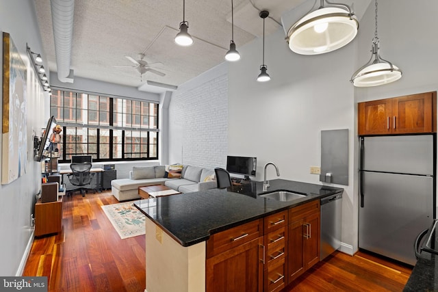 kitchen featuring a peninsula, dark wood-type flooring, a sink, appliances with stainless steel finishes, and dark stone countertops