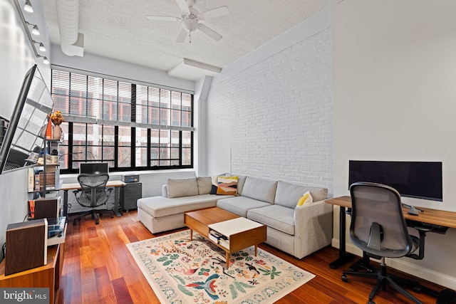 living room with baseboards, a ceiling fan, brick wall, wood finished floors, and a textured ceiling