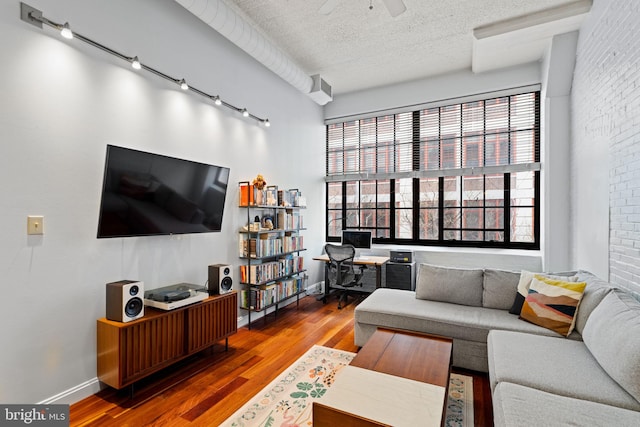 living room with a textured ceiling, brick wall, wood finished floors, a ceiling fan, and baseboards