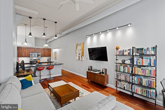 living area with ceiling fan, wood finished floors, a towering ceiling, baseboards, and rail lighting