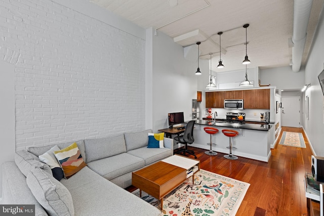 living room featuring dark wood-style floors, brick wall, a towering ceiling, and baseboards