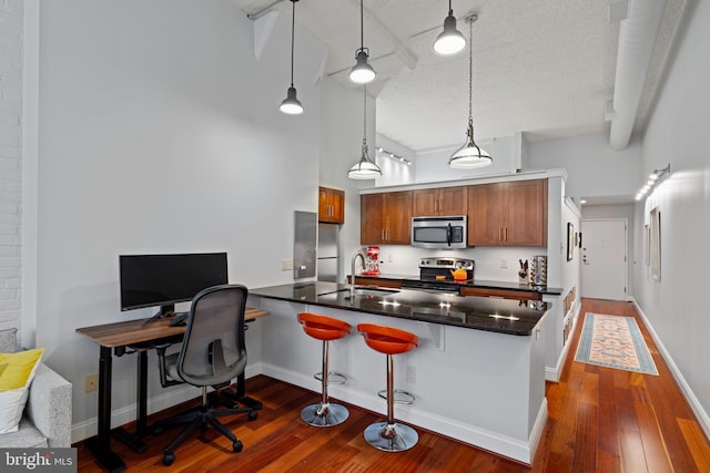 kitchen featuring stainless steel appliances, dark wood-type flooring, a peninsula, a sink, and dark countertops