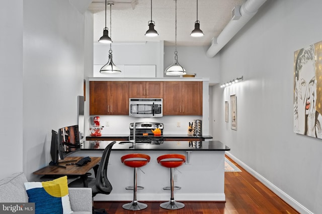 kitchen with a kitchen bar, dark countertops, appliances with stainless steel finishes, a sink, and baseboards