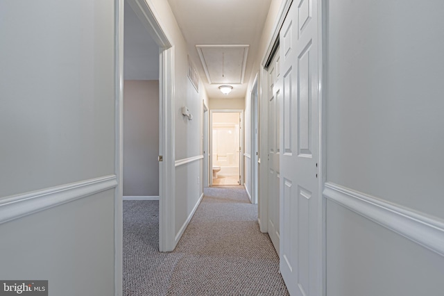 hall with light carpet, attic access, visible vents, and baseboards