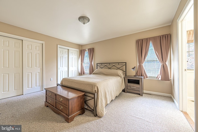 bedroom featuring multiple windows, baseboards, two closets, and light colored carpet