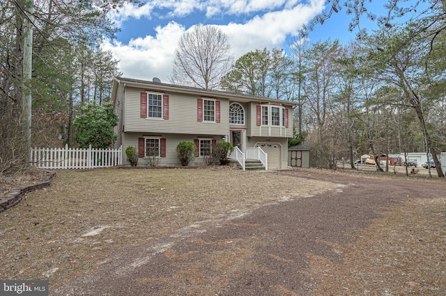 bi-level home featuring dirt driveway, fence, and a garage