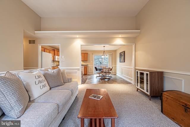 living room featuring a chandelier, light colored carpet, a decorative wall, visible vents, and wainscoting