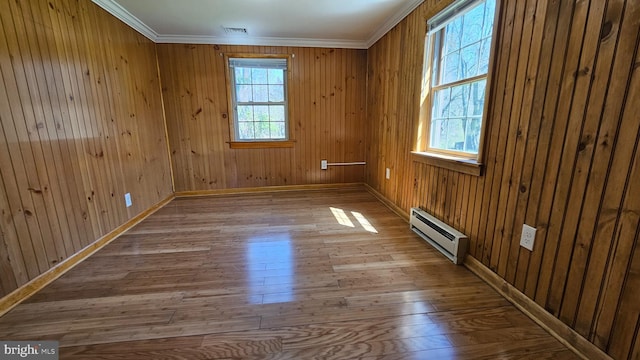 unfurnished room featuring a baseboard heating unit, wood finished floors, a wealth of natural light, and ornamental molding