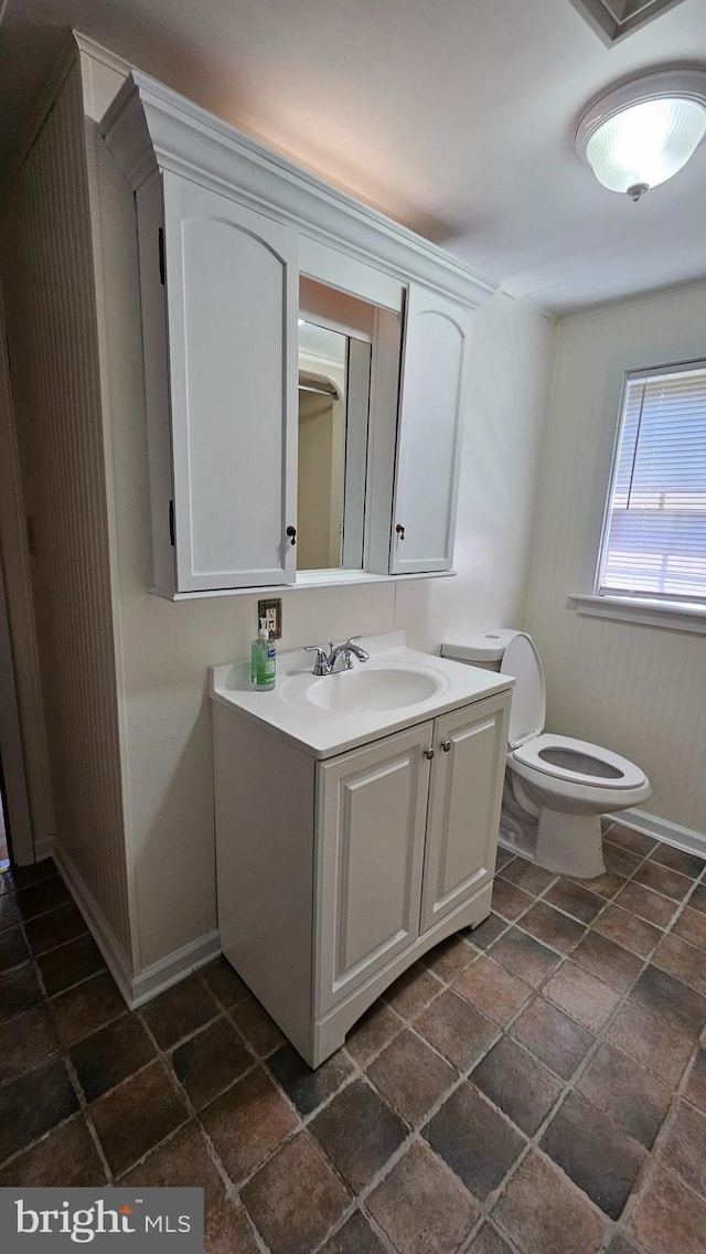 half bathroom featuring stone finish floor, vanity, toilet, and baseboards