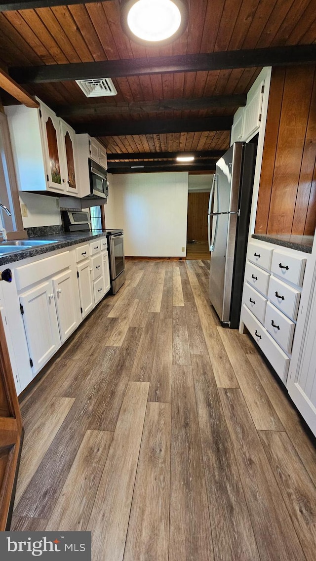 kitchen with stainless steel appliances, dark countertops, visible vents, white cabinetry, and a sink