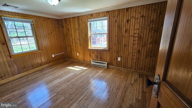 empty room with baseboards, visible vents, a baseboard radiator, wood finished floors, and crown molding