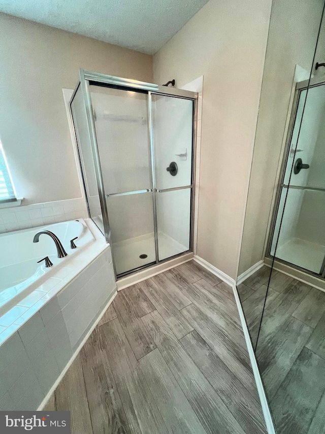 full bathroom with a textured ceiling, a stall shower, wood finished floors, and a bath