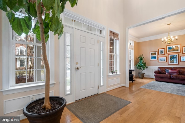 entrance foyer featuring ornamental molding, wainscoting, an inviting chandelier, wood finished floors, and a decorative wall