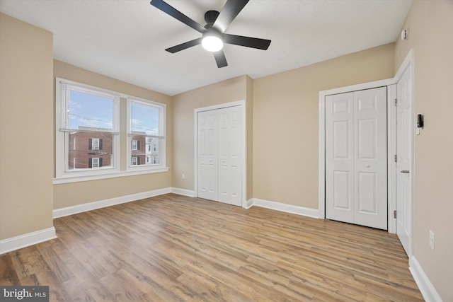 unfurnished bedroom with ceiling fan, two closets, light wood-style flooring, and baseboards