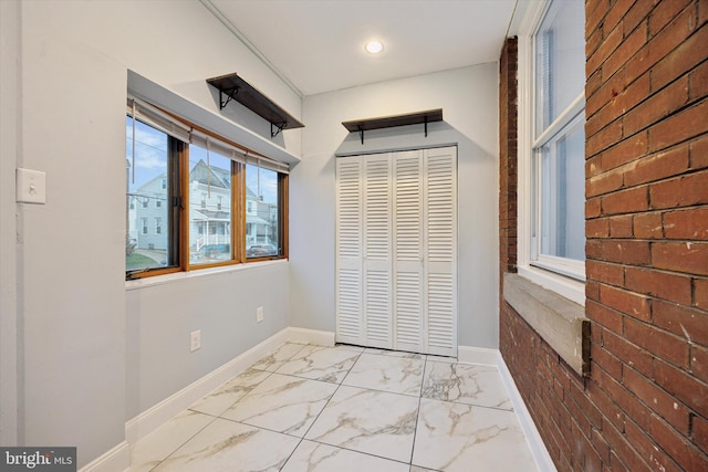 unfurnished bedroom with marble finish floor, brick wall, baseboards, and a closet