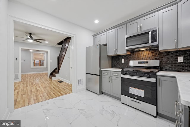 kitchen featuring marble finish floor, stainless steel appliances, light countertops, backsplash, and gray cabinetry