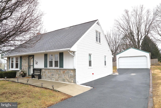 view of front of house with a garage, a shingled roof, stone siding, a chimney, and an outbuilding