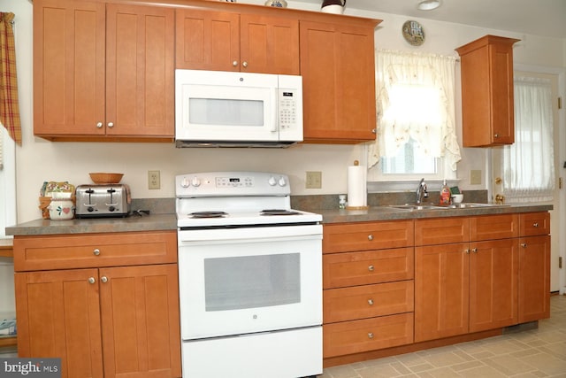 kitchen with dark countertops, white appliances, brown cabinets, and a sink