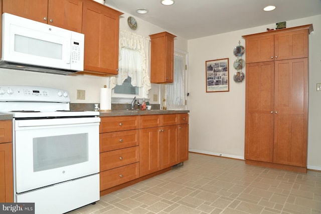 kitchen featuring white appliances, baseboards, brown cabinetry, a sink, and recessed lighting