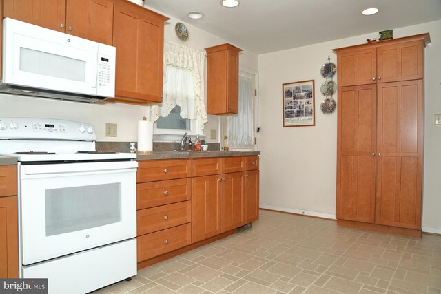 kitchen featuring white appliances, baseboards, brown cabinetry, a sink, and recessed lighting