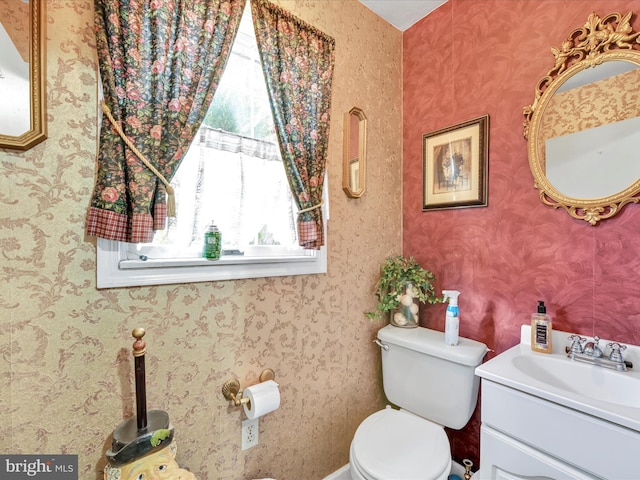 half bath featuring toilet, wallpapered walls, and vanity