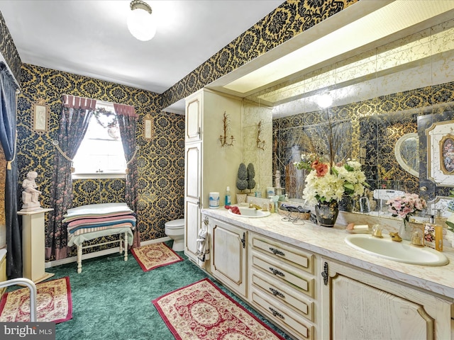 bathroom with double vanity, a sink, toilet, and wallpapered walls