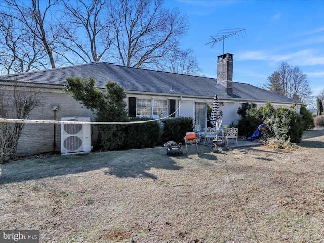 back of property with a shingled roof, brick siding, a patio, and a chimney