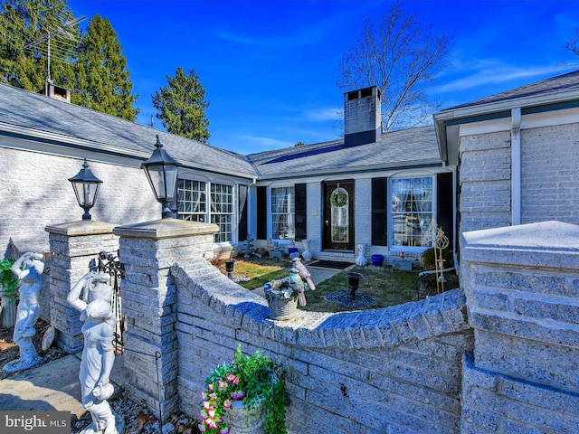 exterior space featuring roof with shingles, a chimney, and brick siding