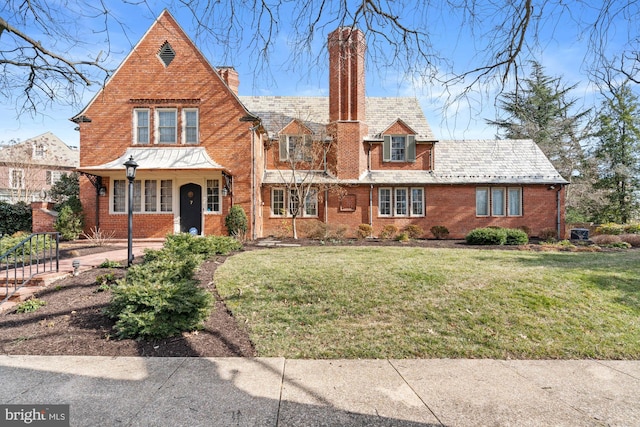 tudor home with brick siding, a chimney, a front yard, and a high end roof