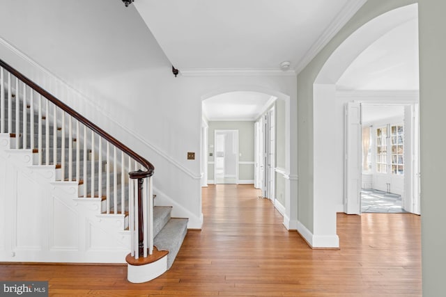 foyer with arched walkways, baseboards, ornamental molding, stairway, and hardwood / wood-style floors