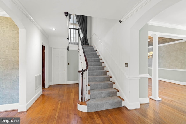 staircase featuring arched walkways, visible vents, crown molding, and hardwood / wood-style floors