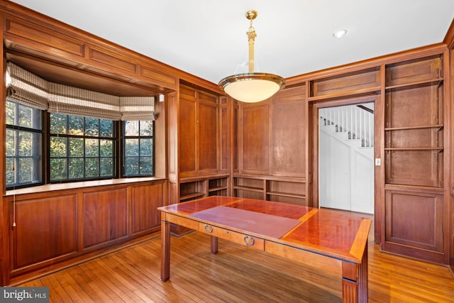 dining area featuring light wood-type flooring, wooden walls, and stairs