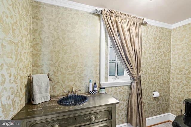 bathroom with baseboards, ornamental molding, a sink, and wallpapered walls