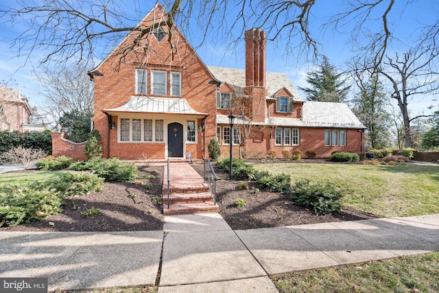 english style home featuring brick siding, a chimney, a front lawn, and a high end roof