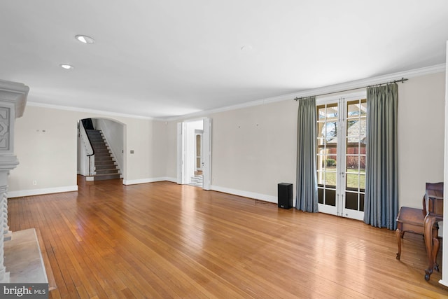 unfurnished living room featuring arched walkways, baseboards, light wood-style flooring, ornamental molding, and stairs