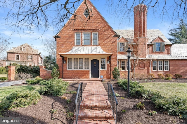 english style home with a high end roof, a chimney, and brick siding