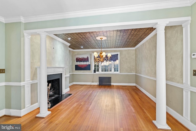 unfurnished living room with decorative columns, radiator heating unit, ornamental molding, baseboards, and hardwood / wood-style flooring