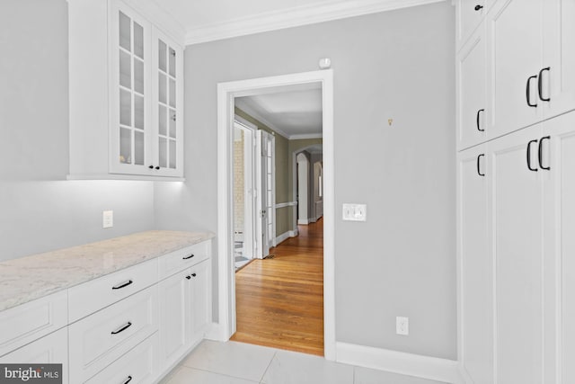 interior space featuring glass insert cabinets, arched walkways, crown molding, and light tile patterned flooring