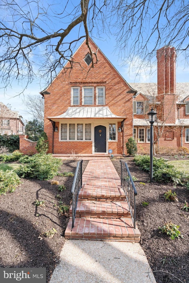 english style home featuring a porch and brick siding