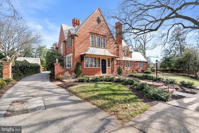 tudor home with driveway, a chimney, fence, a front lawn, and brick siding