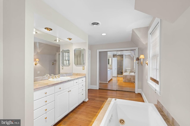 full bath featuring visible vents, vanity, wood finished floors, a jetted tub, and baseboards