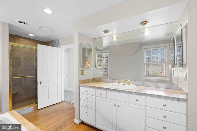 full bathroom with vanity, a stall shower, wood finished floors, and visible vents