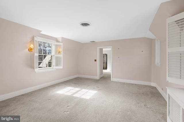 spare room with carpet floors, baseboards, visible vents, and lofted ceiling