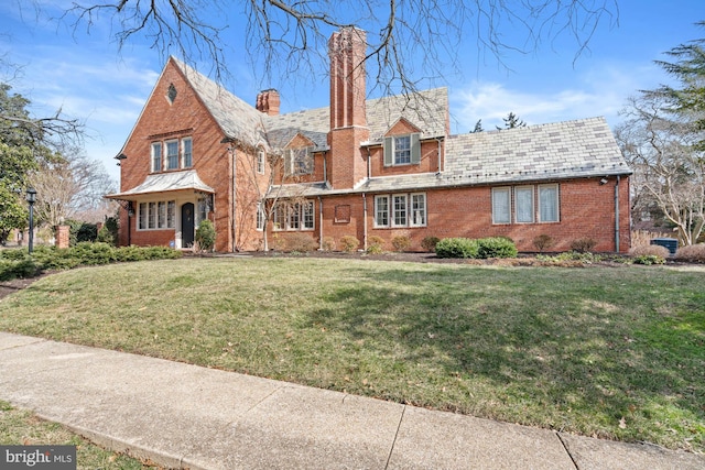 english style home featuring brick siding, a high end roof, a chimney, and a front yard