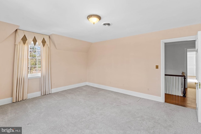 carpeted spare room featuring lofted ceiling, visible vents, and baseboards